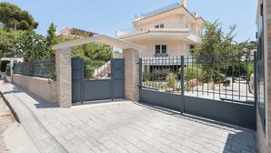 A gated residential property with a paved driveway, a stone wall, and a multi-story building with balconies. - Lagonisi Garden Stay, 10min Walk to Beach (Kalyvia Thorikou)