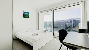 A modern bedroom with a bed, a dining table, and a large window offering a city view. - {Suite 603} Gym, Business Room, Modern, Relax (Lugano)