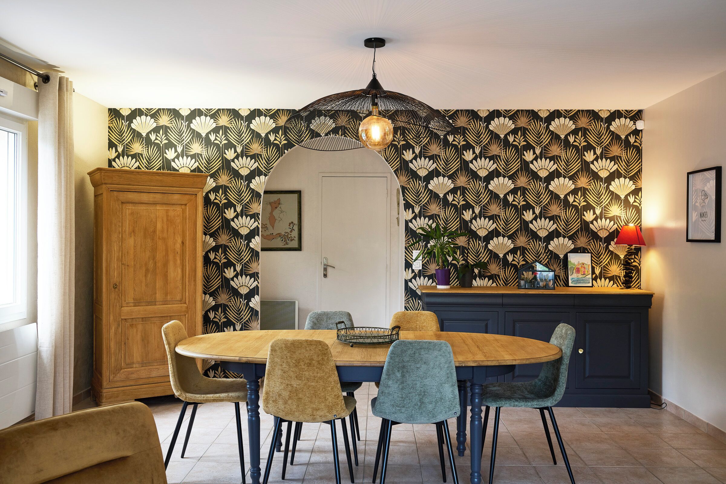Un coin repas comprenant une table ronde en bois, quatre chaises, un buffet et un papier peint à motifs.