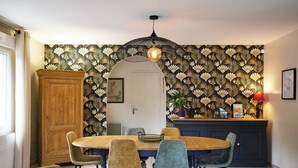 Een eetruimte met een ronde houten tafel, vier stoelen, een kast en behang met een patroon.