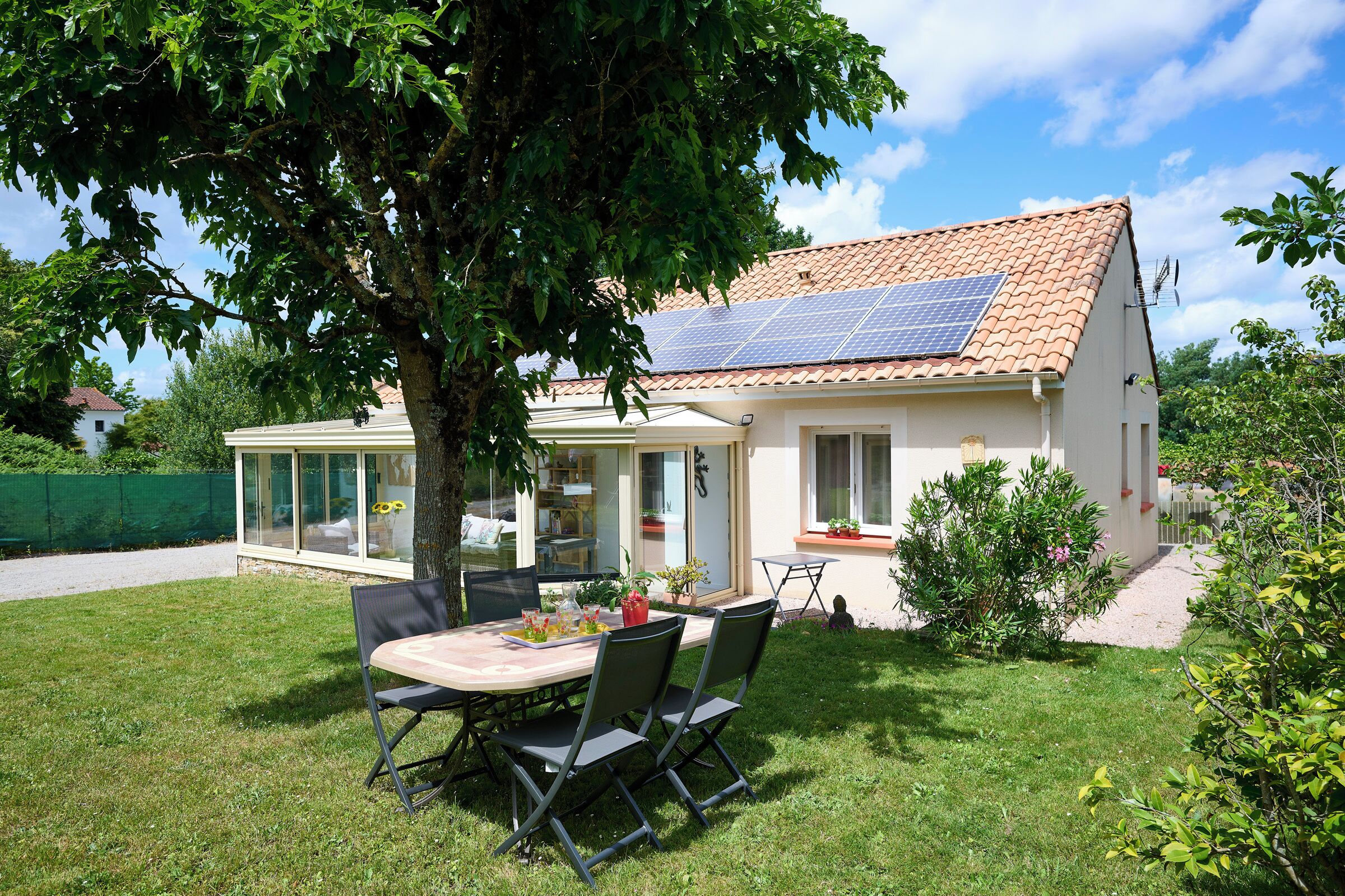 A house with a solar panel roof, a glass-enclosed patio, and a lawn.