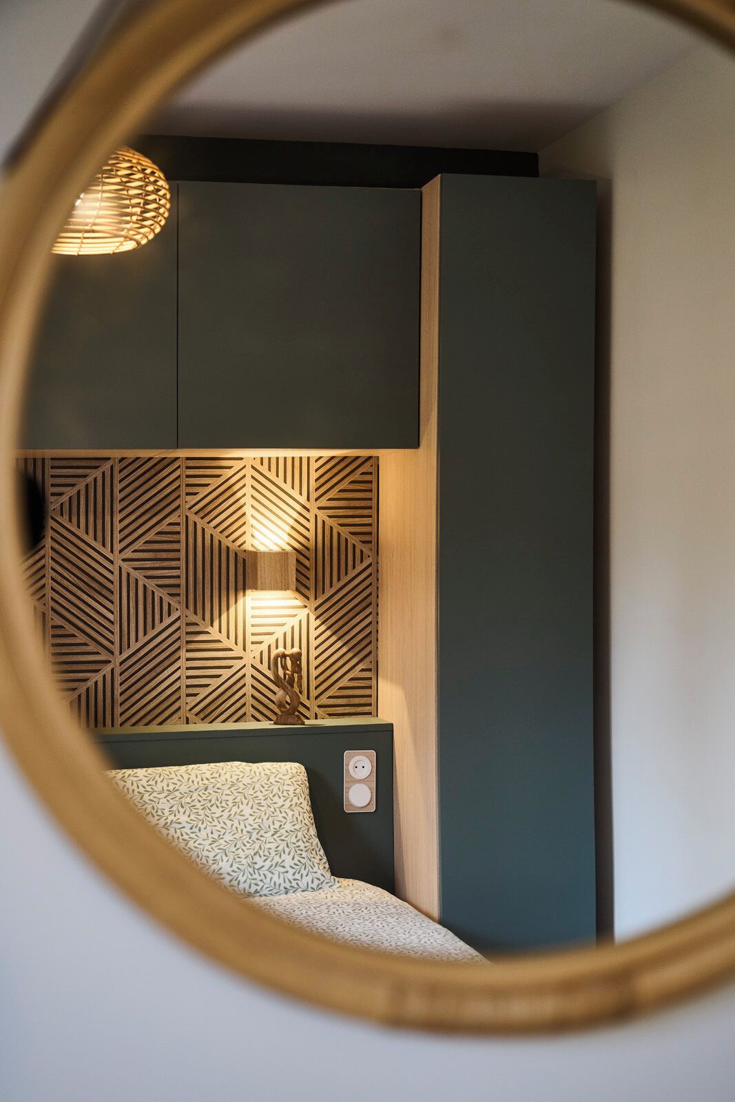 Une chambre à coucher avec une tête de lit à motifs géométriques, une lampe de chevet et un miroir rond.
