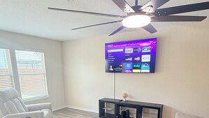 Un salon doté d’un ventilateur de plafond, d’un téléviseur à écran plat fixé au mur et de deux canapés.