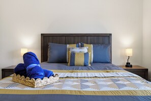 Ein ordentlich bezogenes Bett mit einem gemusterten Überwurf, Kissen und einer blauen Decke. Auf beiden Seiten des Bettes stehen je eine Nachttischlampe.