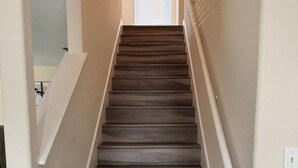 Un escalier avec une rampe, des murs recouverts de moquette et une porte en haut.