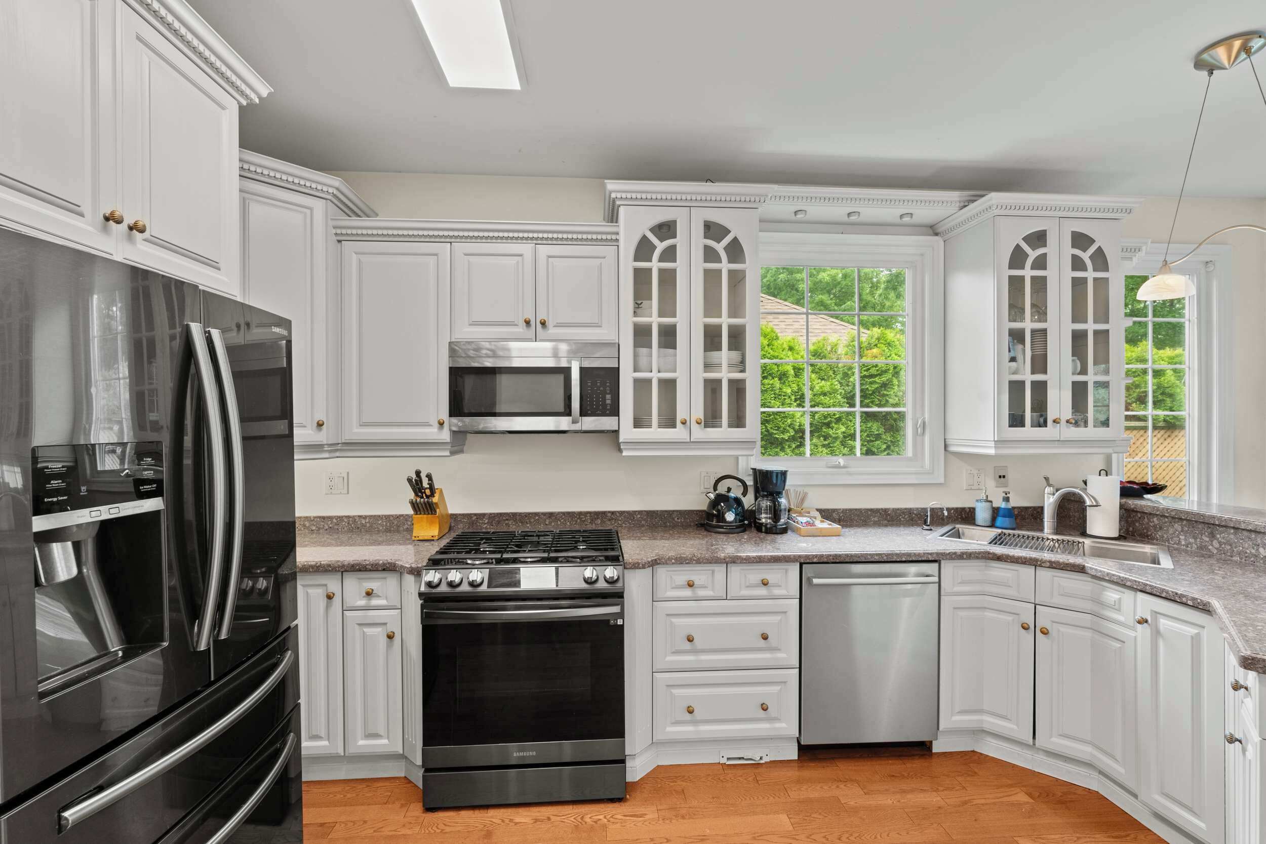 A kitchen with white cabinetry, stainless steel appliances, and a window with a view of greenery.