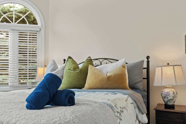 A bed with a white and blue floral bedspread, green and beige pillows, and a blue towel.