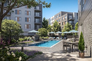 A swimming pool with lounge chairs and umbrellas, surrounded by apartment buildings and greenery.