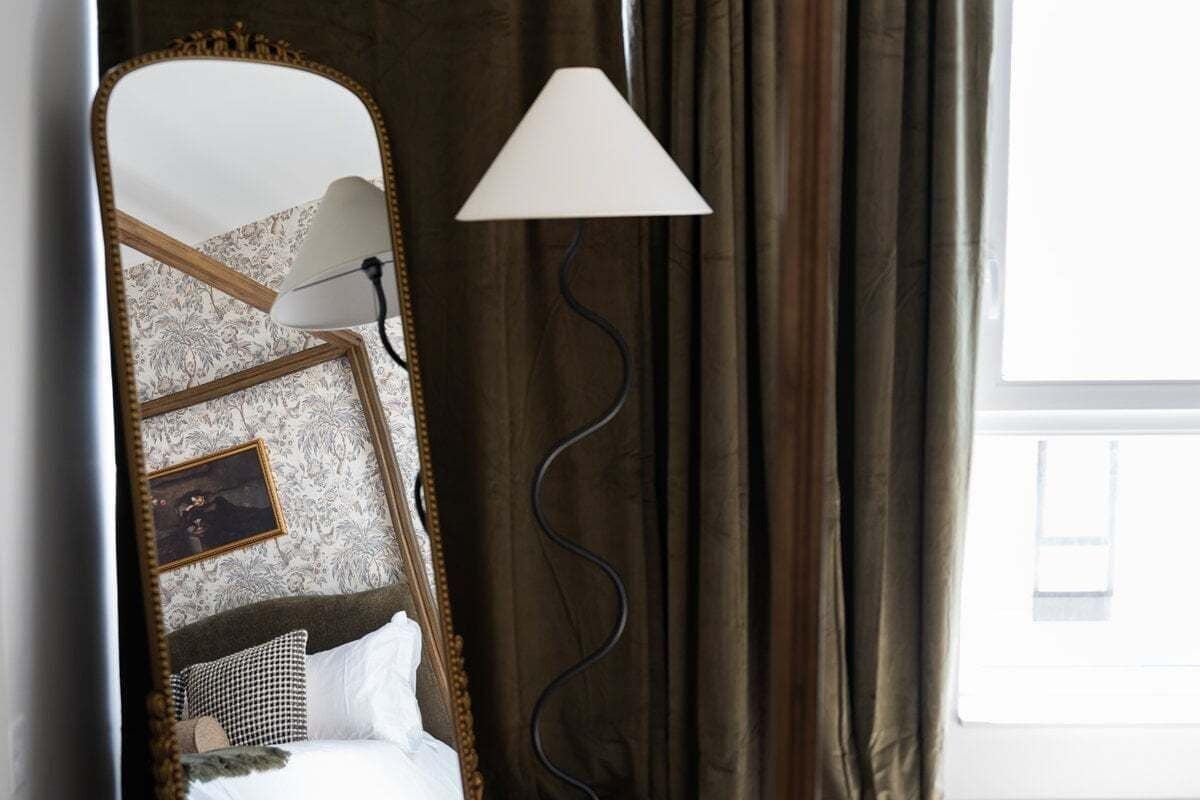 A bedroom with a bed, a mirror, a lamp, and curtains.