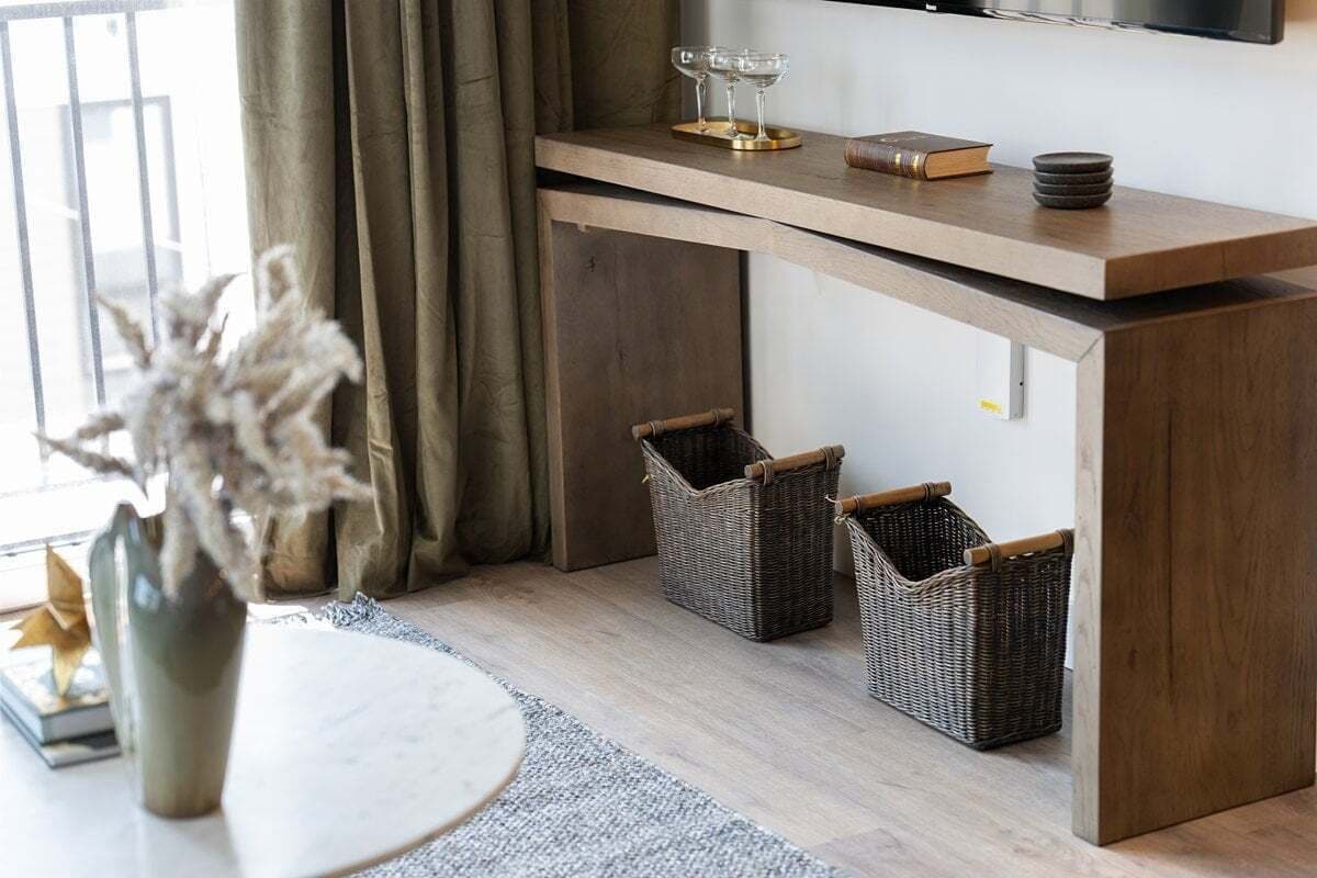 A modern living room with a wooden console table, wicker baskets, a vase with dried flowers, and a round table.