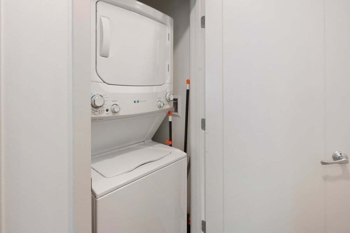 A compact laundry room with a washer and dryer, a door handle, and a towel rack.