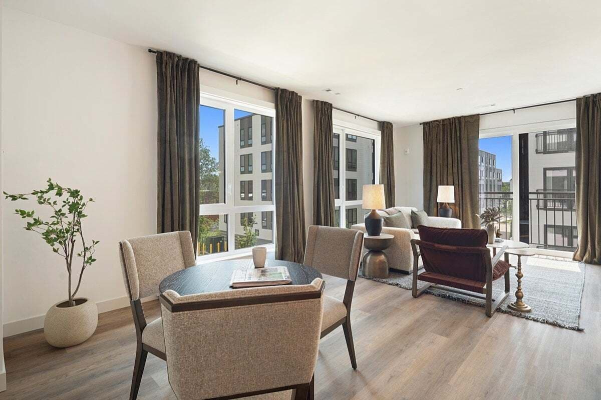 A modern hotel room with a dining area, a sofa, a lamp, and a view of the city.