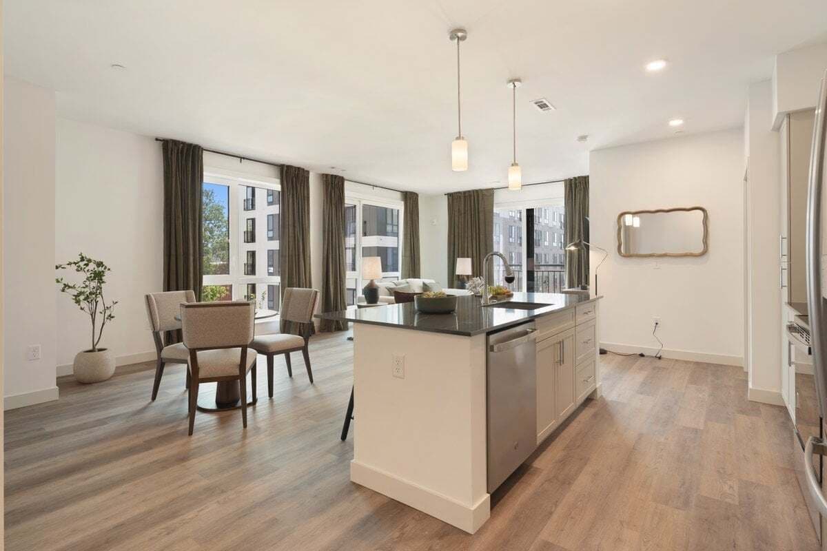 Une cuisine moderne dotée d’un îlot central, d’un coin repas avec des chaises et de grandes fenêtres.