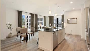 A modern kitchen with a central island, dining area with chairs, and large windows.