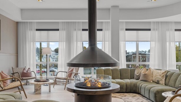 A modern living room with a large fireplace, comfortable seating, and large windows offering a city view. - Hyatus Luxury Residences Salem (Salem)