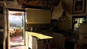 Une cuisine avec des meubles blancs, un pare-feu en carreaux, une lanterne suspendue et une vue sur l’extérieur par une porte ouverte.