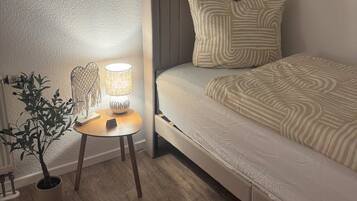 A bedroom with a sloped ceiling, a bed with striped bedding, a bedside table with a lamp, and a potted plant.