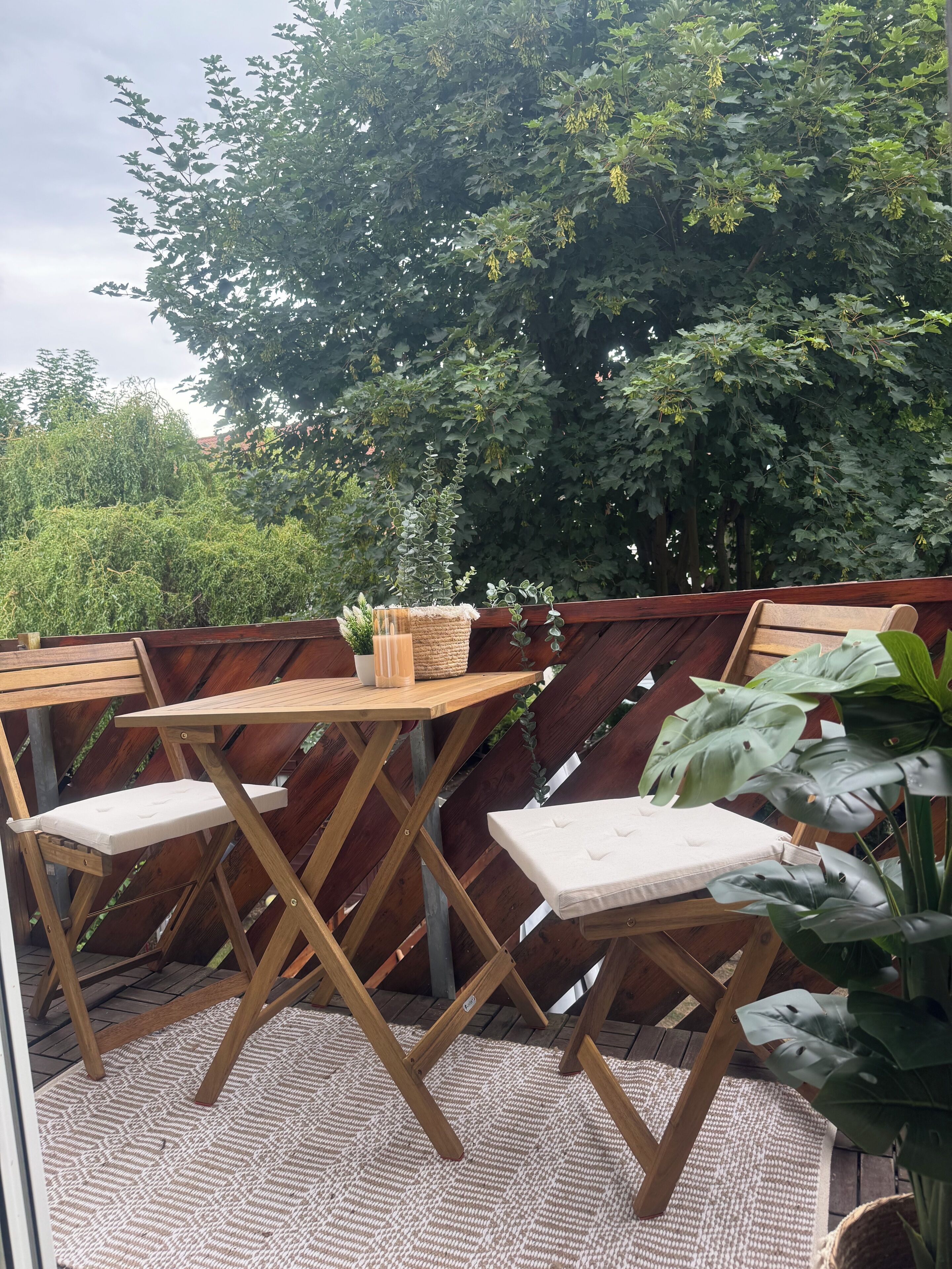 Una terraza de madera con una mesa y sillas, rodeada por un cerco de madera y abundante vegetación.
