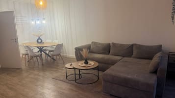 A living room with a sofa, a coffee table, a dining table with chairs, and a pendant light.