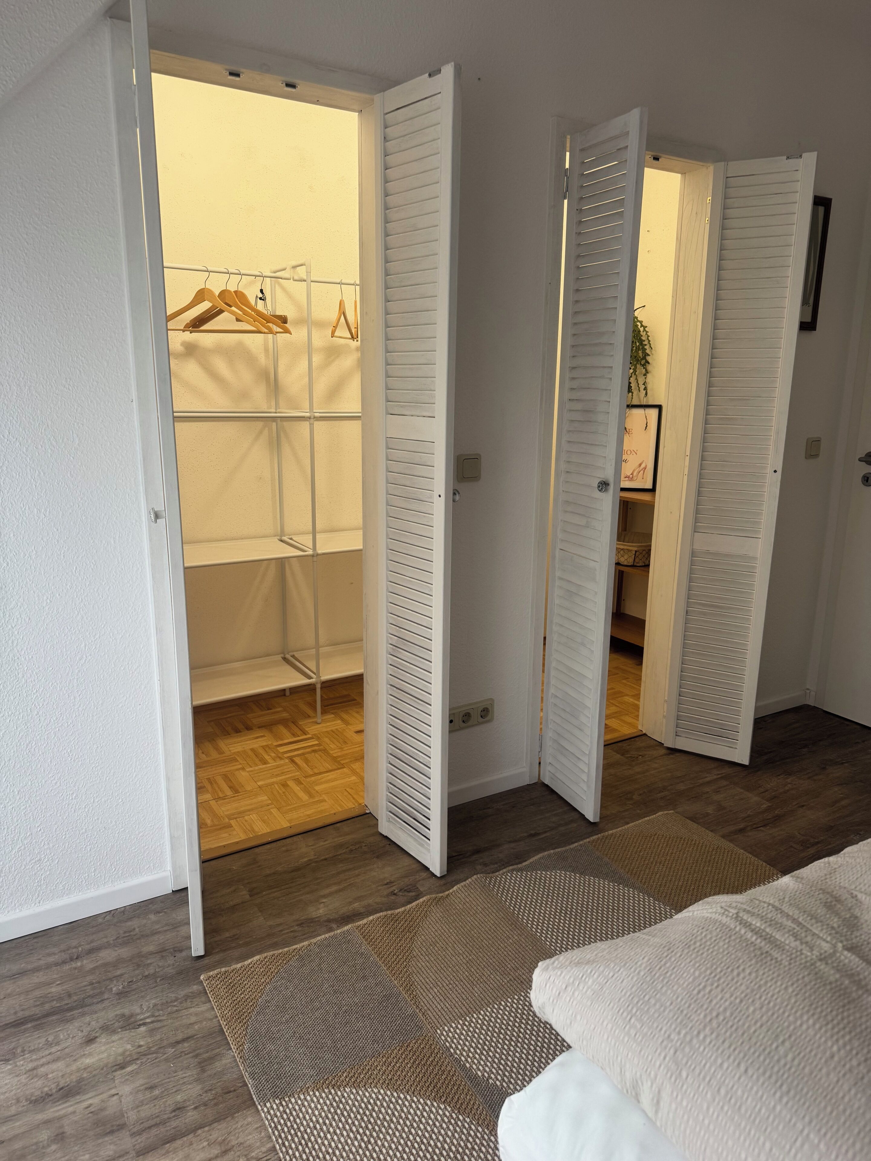 Una stanza con pavimento in legno, un letto bianco e un armadio con le ante aperte.