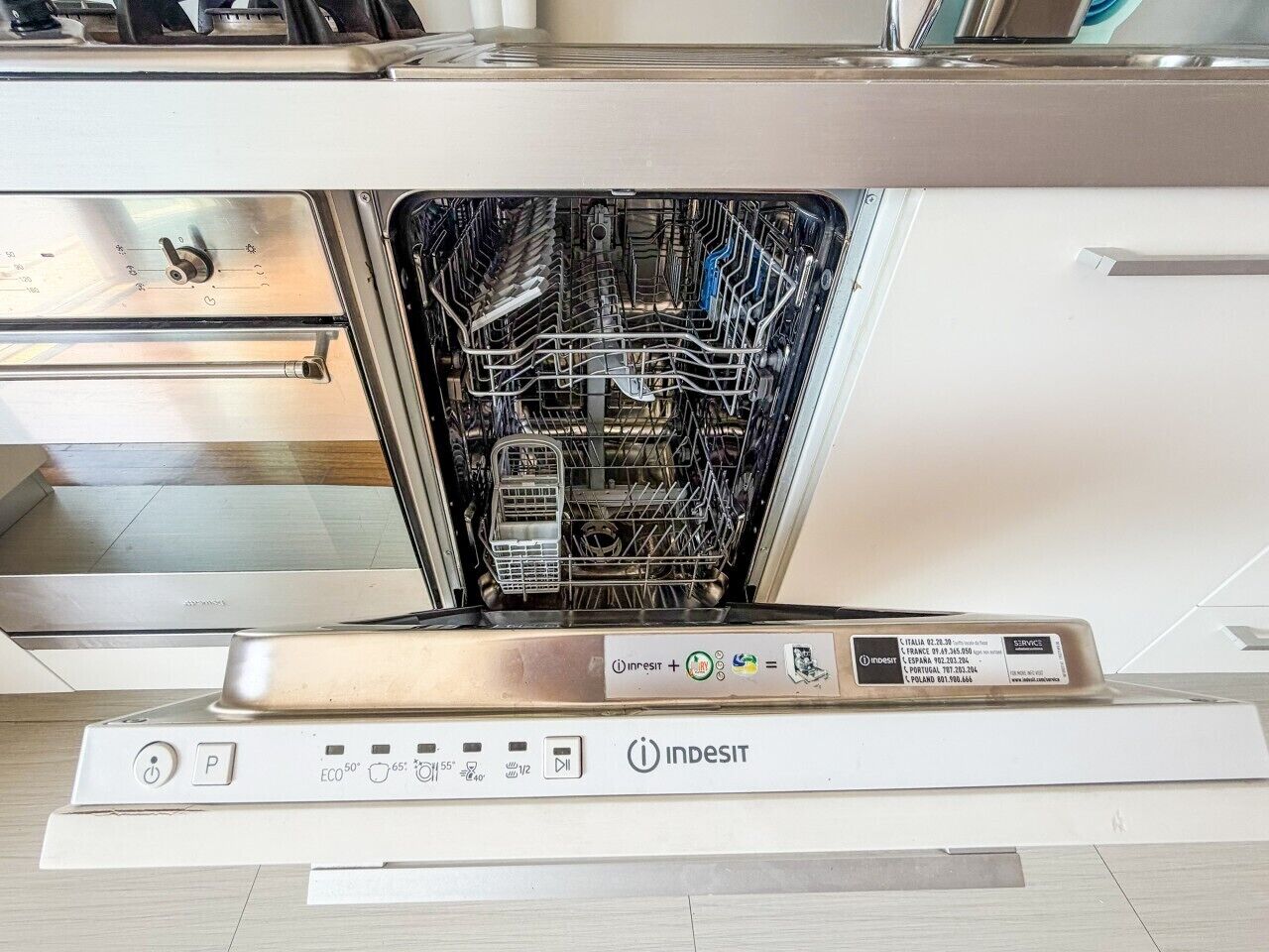A modern kitchen with an open dishwasher, a stainless steel range hood, and a control panel with various settings.