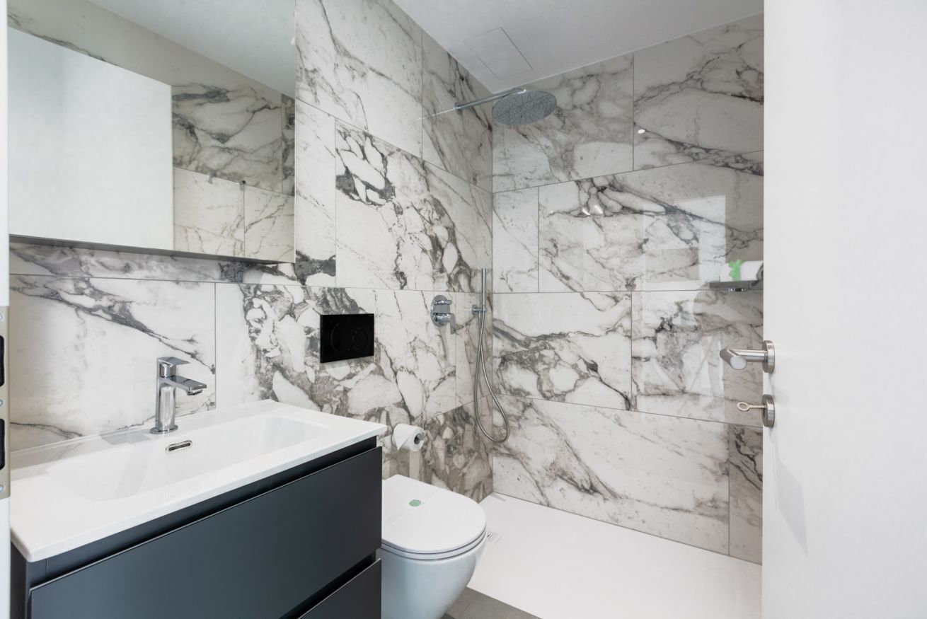 Un baño con pared de mármol, lavamanos, inodoro y ducha.