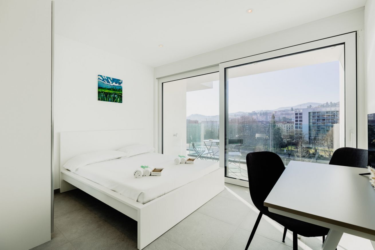 Un dormitorio moderno con cama, una mesa de comedor y un ventanal que ofrece vista a la ciudad.