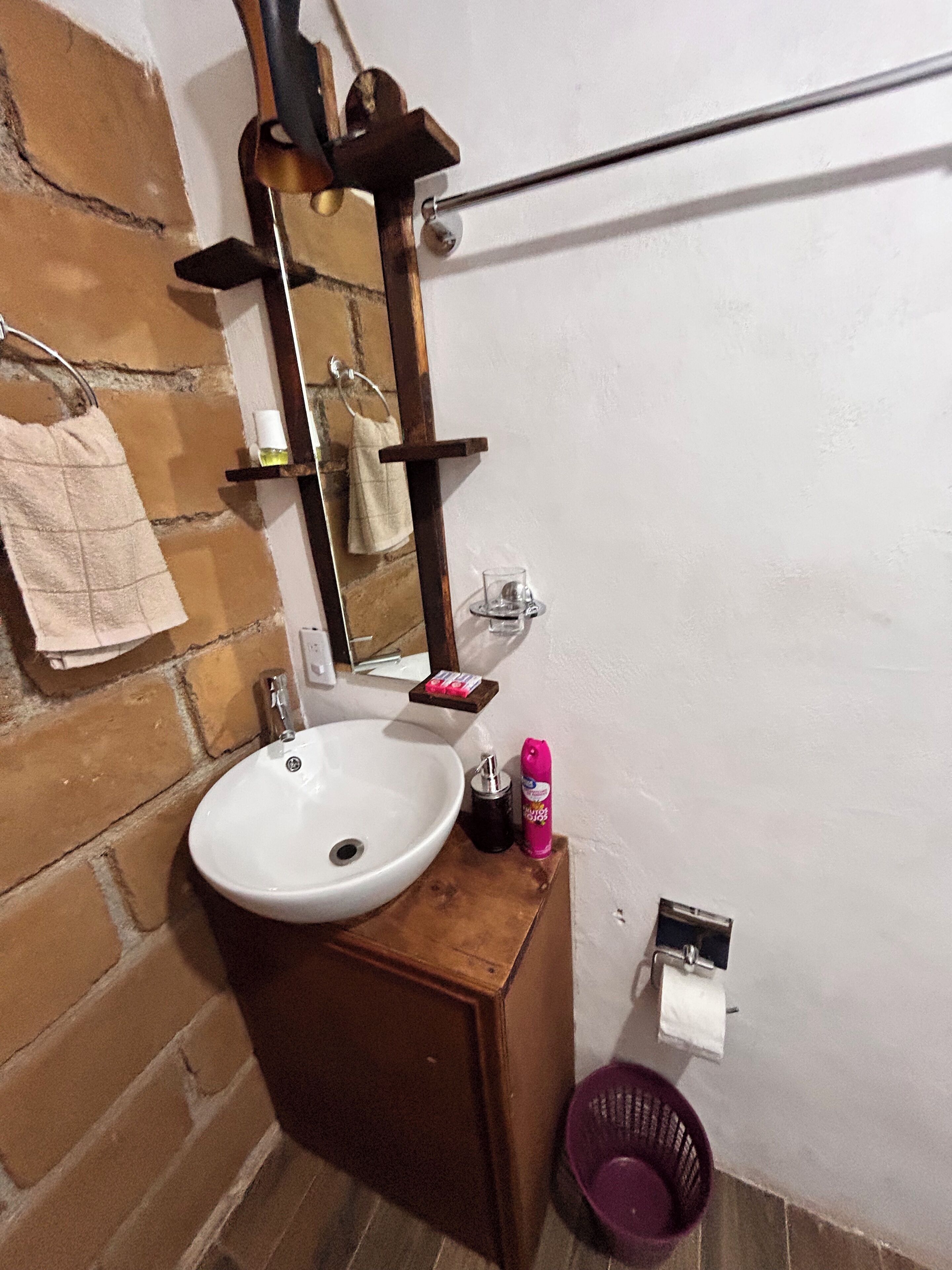 Un baño con un lavamanos blanco, un armario de madera, un espejo, un perchero para toallas y un dispensador de jabón.