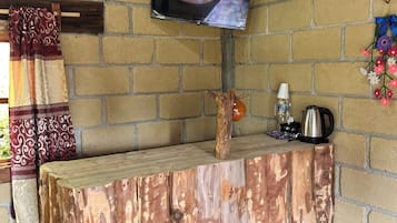 Une pièce rustique avec une table en bois, un téléviseur fixé au mur et un lit recouvert d’une courtepointe aux couleurs vives.