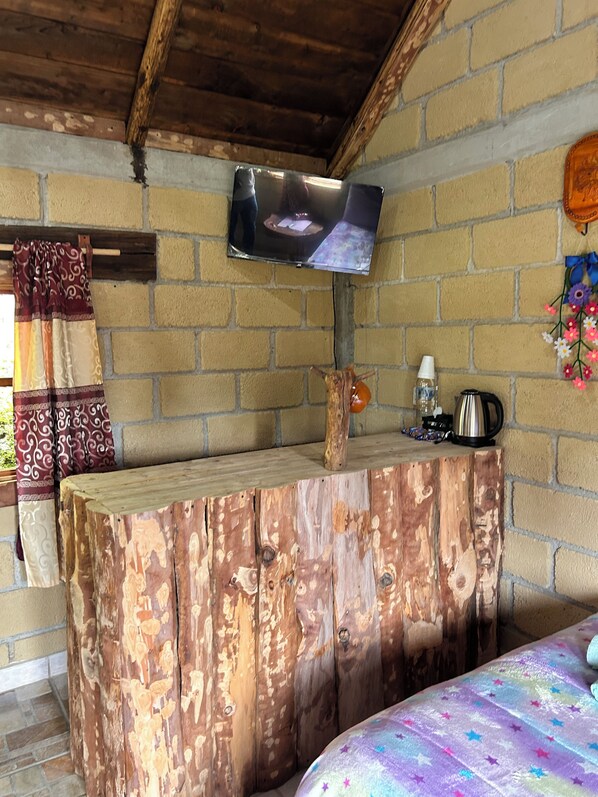 A rustic room with a wooden table, a television mounted on the wall, and a bed with a colorful bedspread.