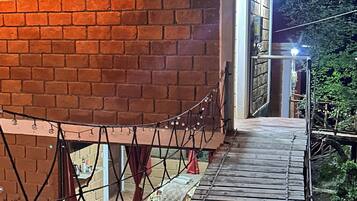 Un bâtiment en briques avec une terrasse en bois menant à une porte, le tout entouré de verdure.