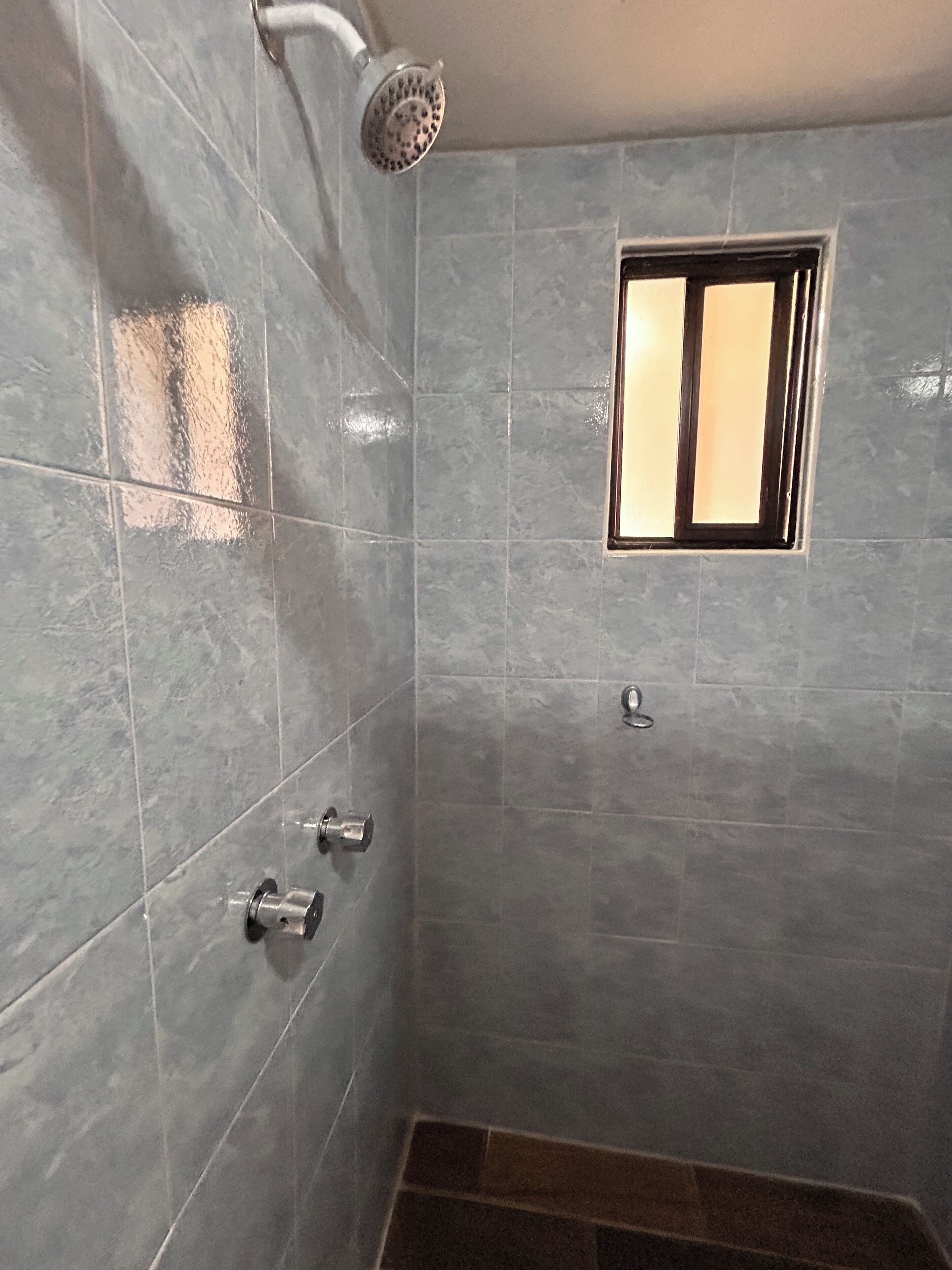 Un baño con baldosas grises, un cabezal de ducha, una ventana y un inodoro.