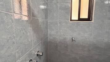 Un baño con baldosas grises, un cabezal de ducha, una ventana y un inodoro.