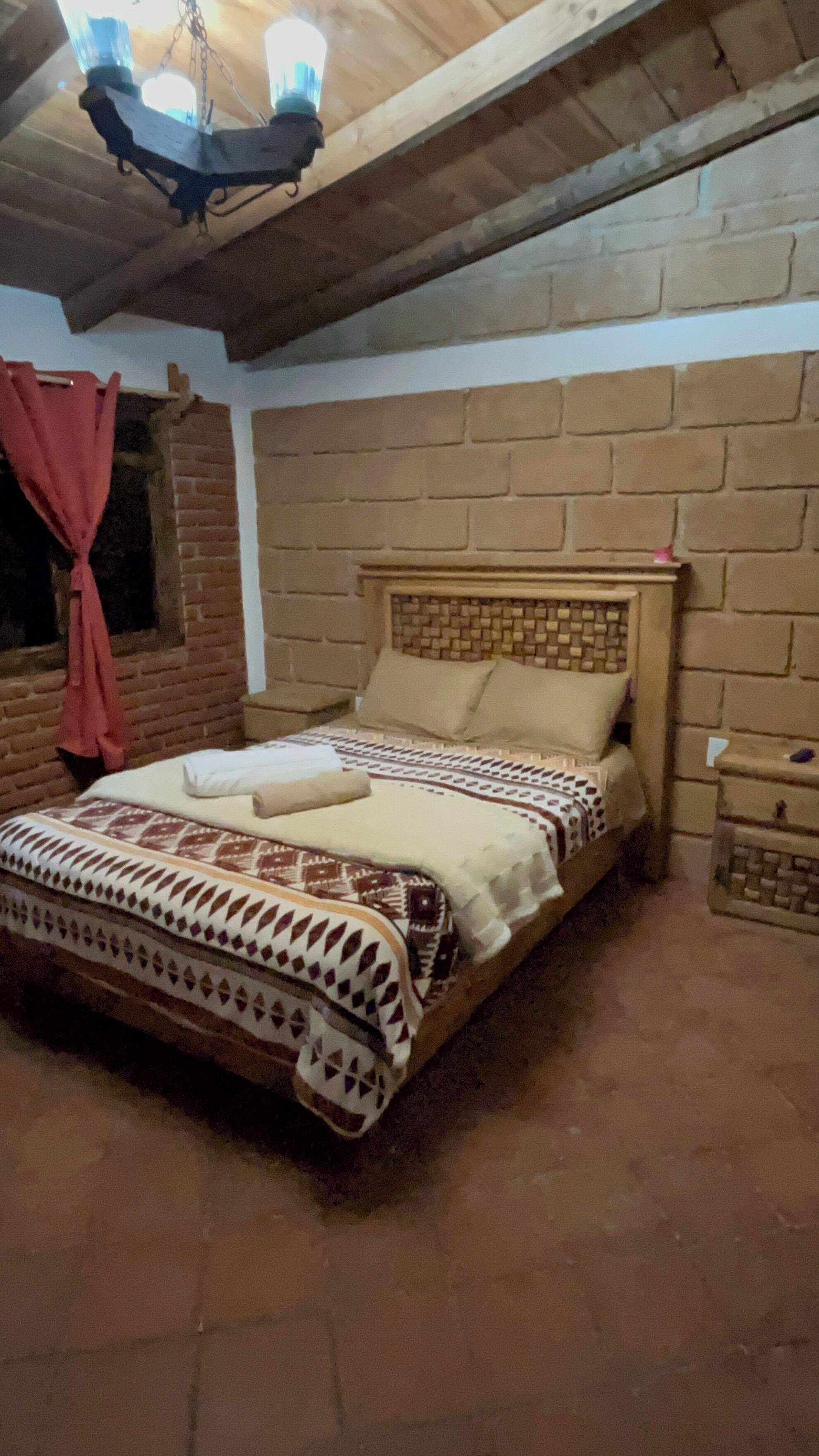 Una cama individual con un edredón estampado, cabecera de madera y pared de ladrillo al fondo.