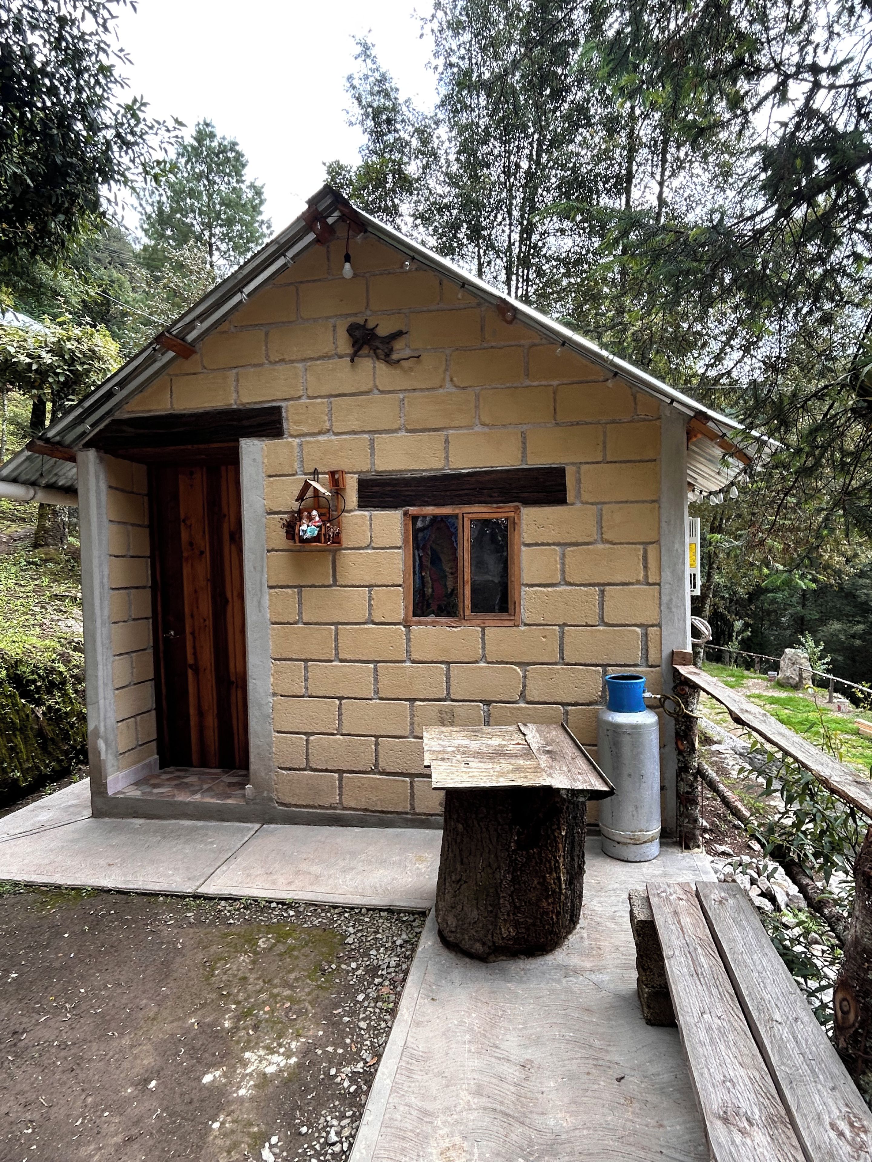 Un pequeño edificio de piedra con puerta de madera, una banca y un bote de basura.