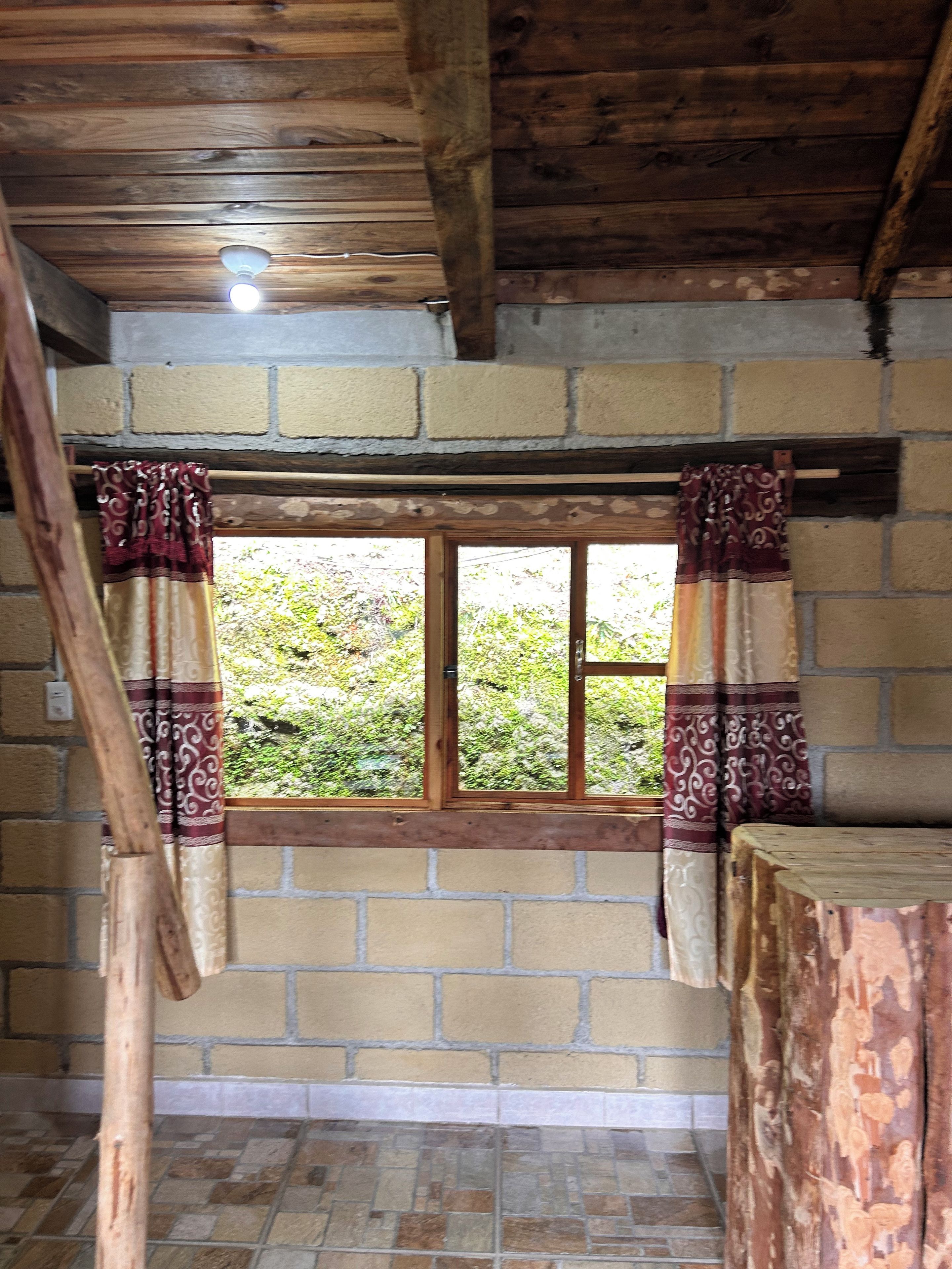 Una habitación con ventana, vigas de madera y pared de ladrillo.