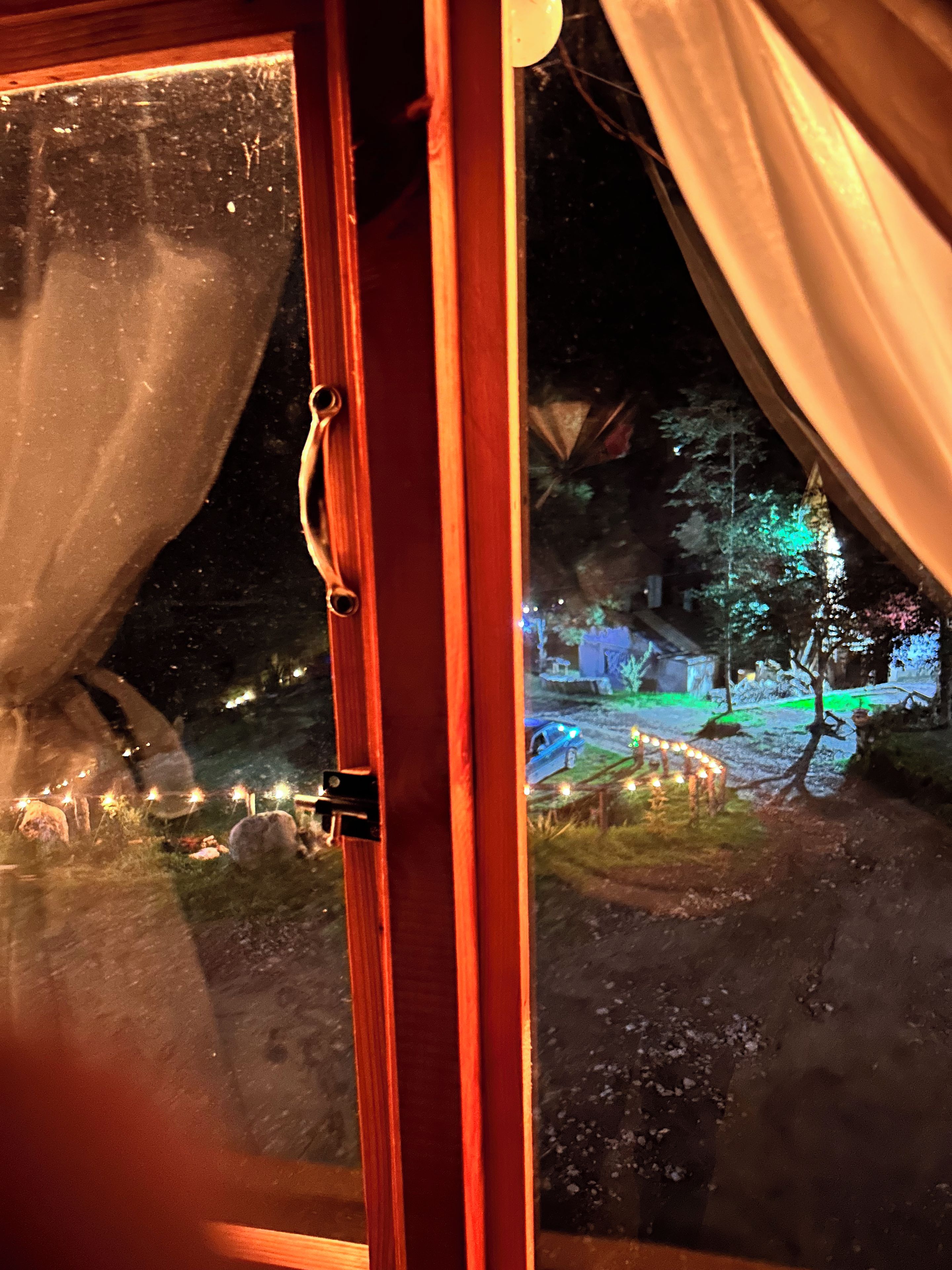 A window with a view of a nighttime outdoor scene, including a car and lights.