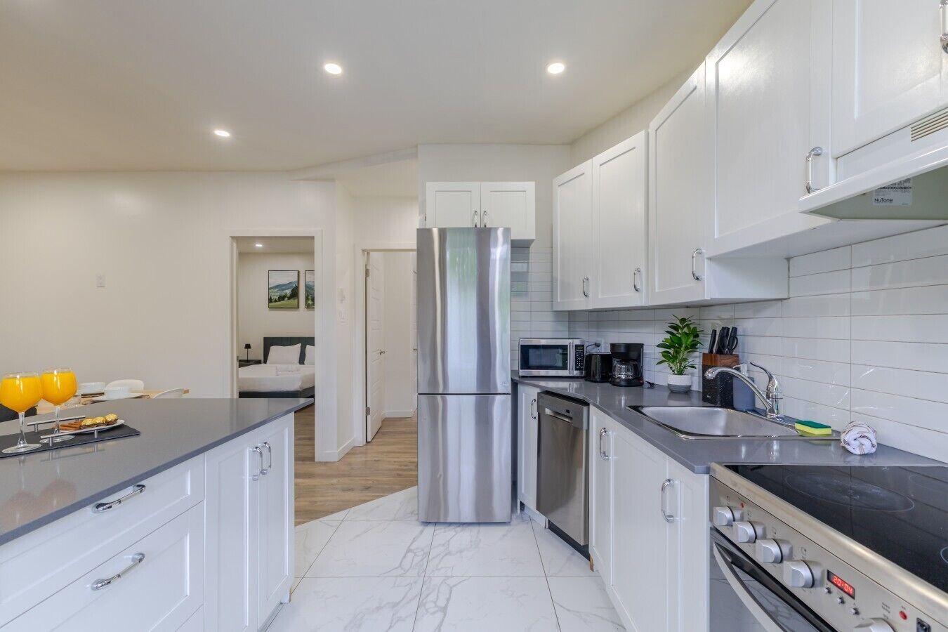 A modern kitchen with stainless steel appliances, a marble countertop, and white cabinetry.