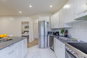 A modern kitchen with stainless steel appliances, a marble countertop, and white cabinetry. - The Quiet Corner | Heart of Montréal 2B1B (Montreal)