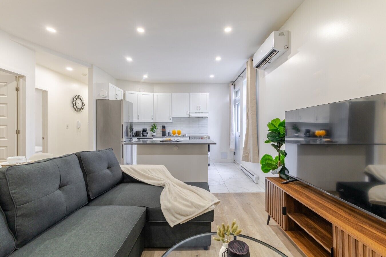 A modern living room with a grey sofa, a glass coffee table, and a flat-screen TV on a wooden stand.
