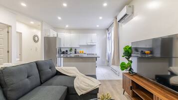 A modern living room with a grey sofa, a glass coffee table, and a flat-screen TV on a wooden stand.