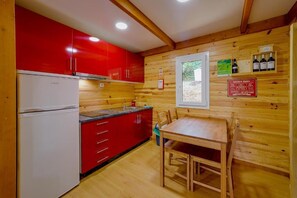 Una cocina compacta con armarios rojos, un refrigerador blanco y una mesa de comedor de madera.