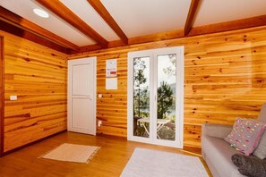 Una habitación con paneles de madera y una puerta corrediza de vidrio que da a un espacio exterior, un sofá con cojines y una pequeña alfombra en el suelo.