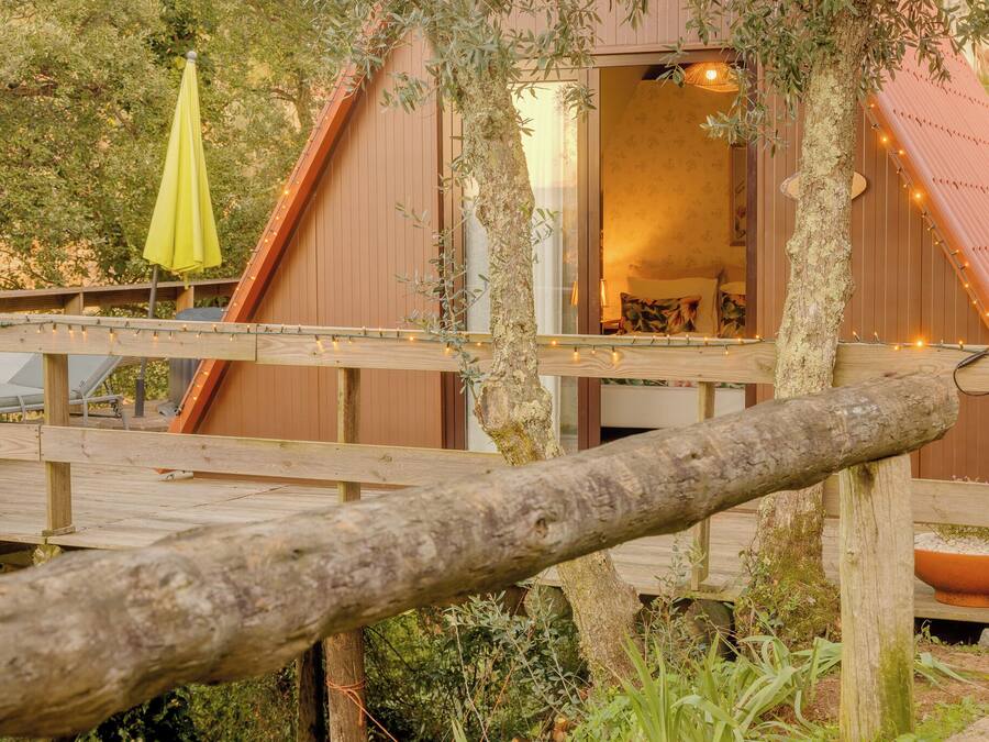 A wooden deck with a rustic tree trunk in the foreground, a wooden building with a window, and a yellow umbrella.