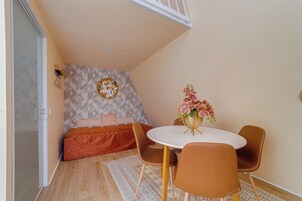 Una habitación pequeña y acogedora con cama, una mesa redonda con sillas, un adorno en la pared y una planta en maceta.