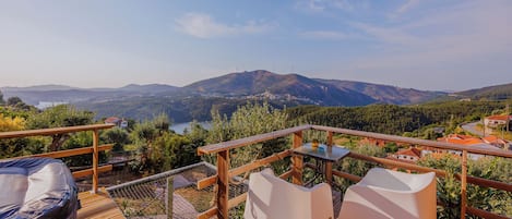 A wooden deck with white chairs and a table overlooking a mountainous landscape with wind turbines.