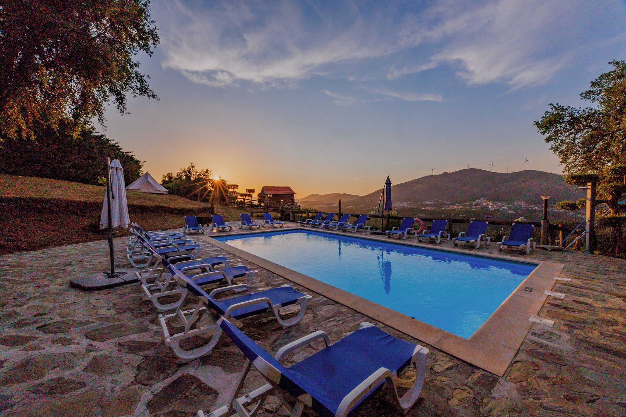 Una piscina con sillas de descanso y vistas a la puesta de sol y montañas.