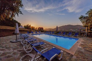 Una piscina con sillas de descanso y vistas a la puesta de sol y montañas.