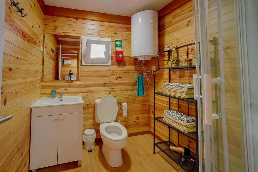 Une salle de bain aux murs lambrissés, équipée de toilettes, d’un lavabo et d’une étagère où sont rangées les serviettes.