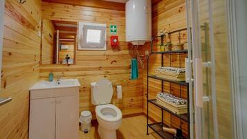Une salle de bain aux murs lambrissés, équipée de toilettes, d’un lavabo et d’une étagère où sont rangées les serviettes.